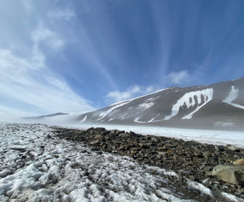 Low-angle shot of a windswept glacier with rocky surface and clear blue sky.