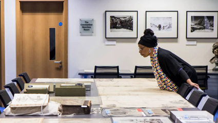 A person looking at historic materials, including maps, books, and photographs spread out on a large table.