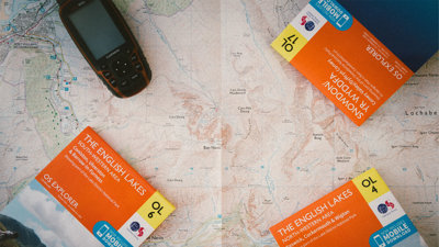 Closed Ordnance Survey maps titled English Lakes laying on top of an open map.