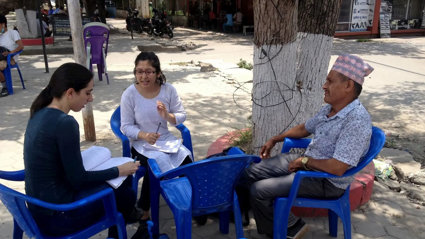 Three people sat on blue plastic chairs in a circle conversing and taking notes.