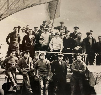 A sepia image of Ernest Shackleton and the crew of Endurance, standing on the ship with sails in the background