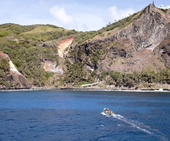 A coastal cliff landscape covered in grassy vegetation with a motor boat moving towards the cliffs.