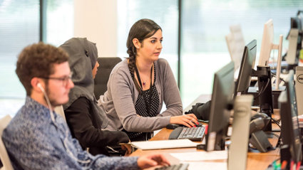 Three people working at a desk and looking at computer screens.