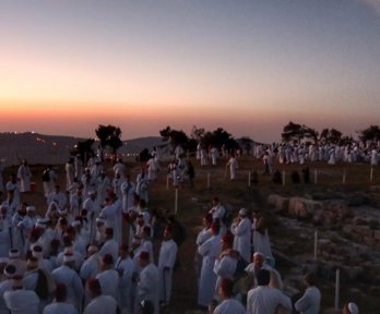 A large group of people gathered for a ceremony on a mountaintop as the sun is setting.