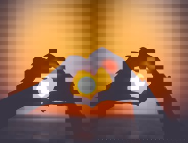 Silhouette of a persons hands making a heart shape around the sun