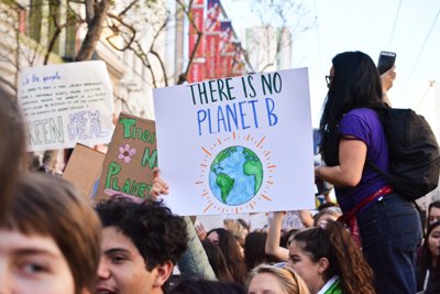 Protesters walk down an urban highstreet holding placards. The placard furthest to the front says 'There is no planet B'