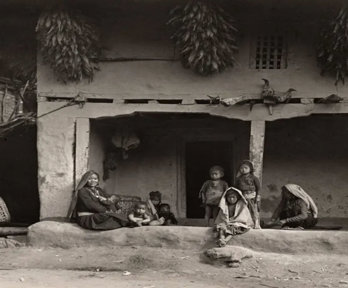 Black and white photograph of a group of Indigenous people sitting in front of a typical Limbu House in Eastern Nepal.