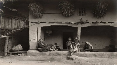 Black and white photograph of a group of Indigenous people sitting in front of a typical Limbu House in Eastern Nepal.