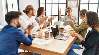 Group of people sat around a table clapping and congratulating colleague