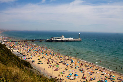 A view over a beach packed with people with a pier jutting out into the sea