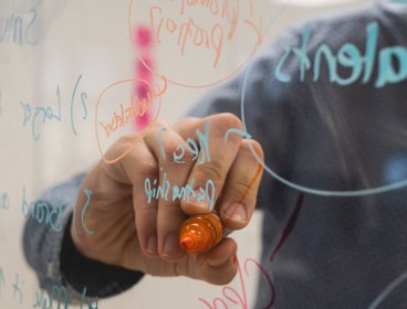 Person writing on a glass board with a felt-tip pen. 