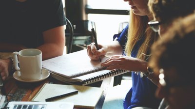 Group of people sat around a table with one person writing notes in a notebook