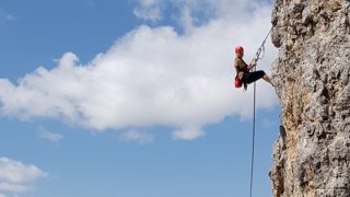 Woman in rock climbing gear ascending a rock.