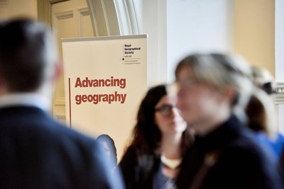 Banner with the text 'Advancing geography' and the Society's logo, with blurred figures in the foreground 