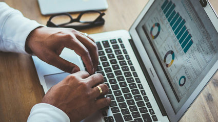 Person typing on a laptop keyboard with graphs on the screen. 